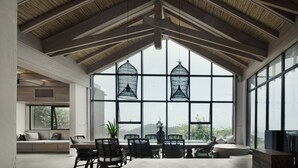 Een ruime kamer met een hoge plafond, grote ramen en een zithoek met een tafel en stoelen.