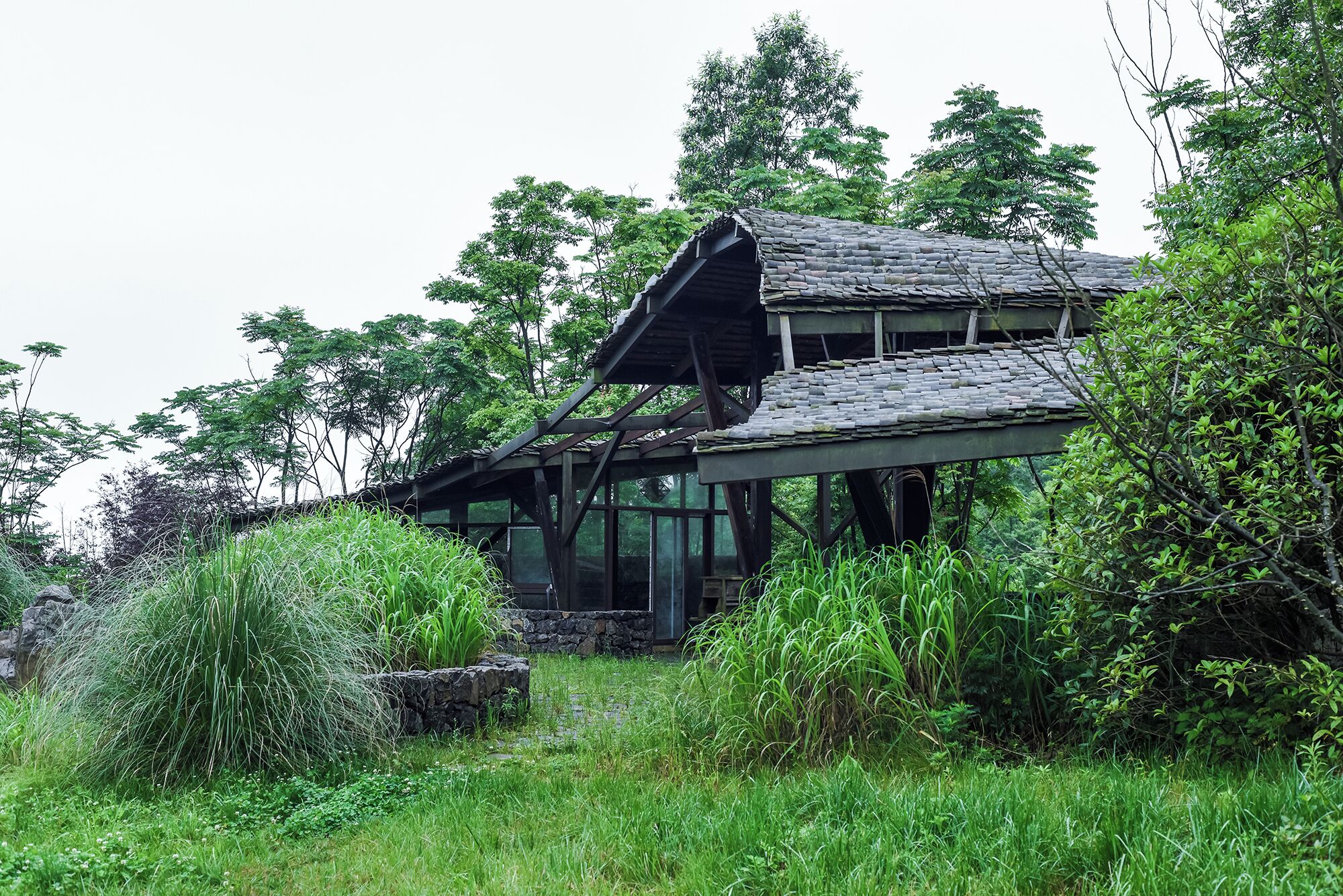 A rustic cabin with a sloped roof, surrounded by lush greenery and trees.