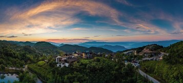 Vista panorâmica de uma aldeia montanhosa com arquitetura tradicional, uma estrada sinuosa e um lago.