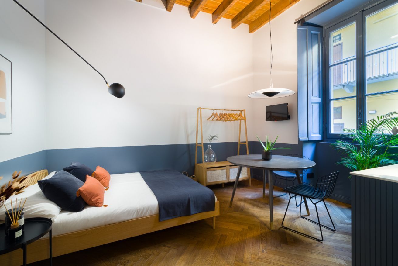 Une chambre moderne comprenant un lit, une table de chevet, un portant à vêtements et une petite table ronde avec des chaises.