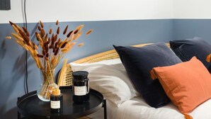 A bedroom with a bed, pillows, a bedside table with candles, and a vase with dried plants. - Design studio of wood & charm (Milano)