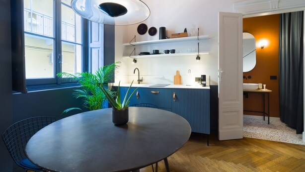 A modern kitchen with blue cabinets, a round dining table, and a potted plant. - Design studio of wood & charm (Milano)