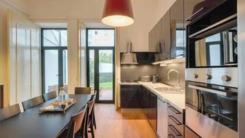 A modern kitchen with a dining area, featuring a large window, stainless steel appliances, and a red pendant light.