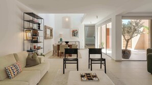 Un soggiorno moderno con un divano, poltrone, un tavolino da caffè e una libreria. Sullo sfondo, una zona pranzo con tavolo e sedie.