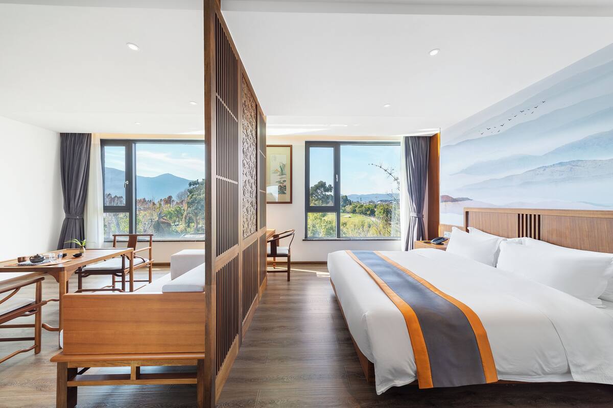 A hotel room with a large bed, a desk, a chair, and a view of mountains through large windows.