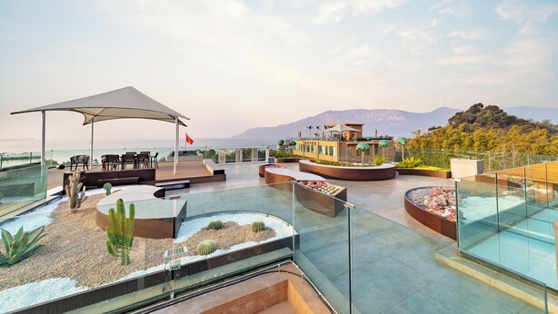 A rooftop terrace with seating, a pool, and a view of the sea and mountains.
