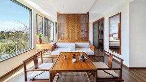 A modern hotel room with a wooden dining table, cushioned seating, a large window with a view, and traditional decor elements.