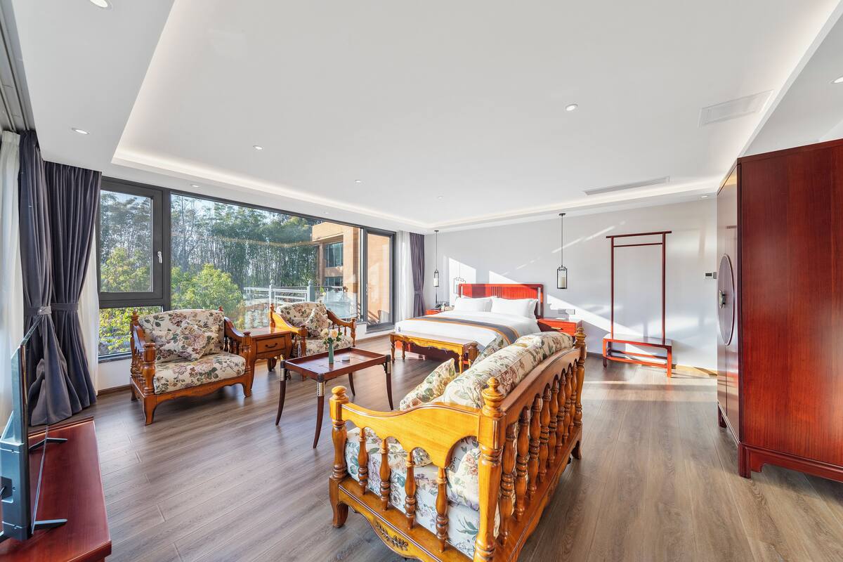 A spacious bedroom with a large bed, a wooden sofa, and a desk.