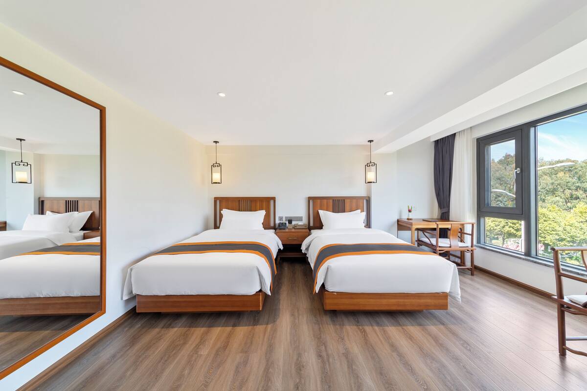 A hotel room with two beds, a desk, and a large window offering a view.