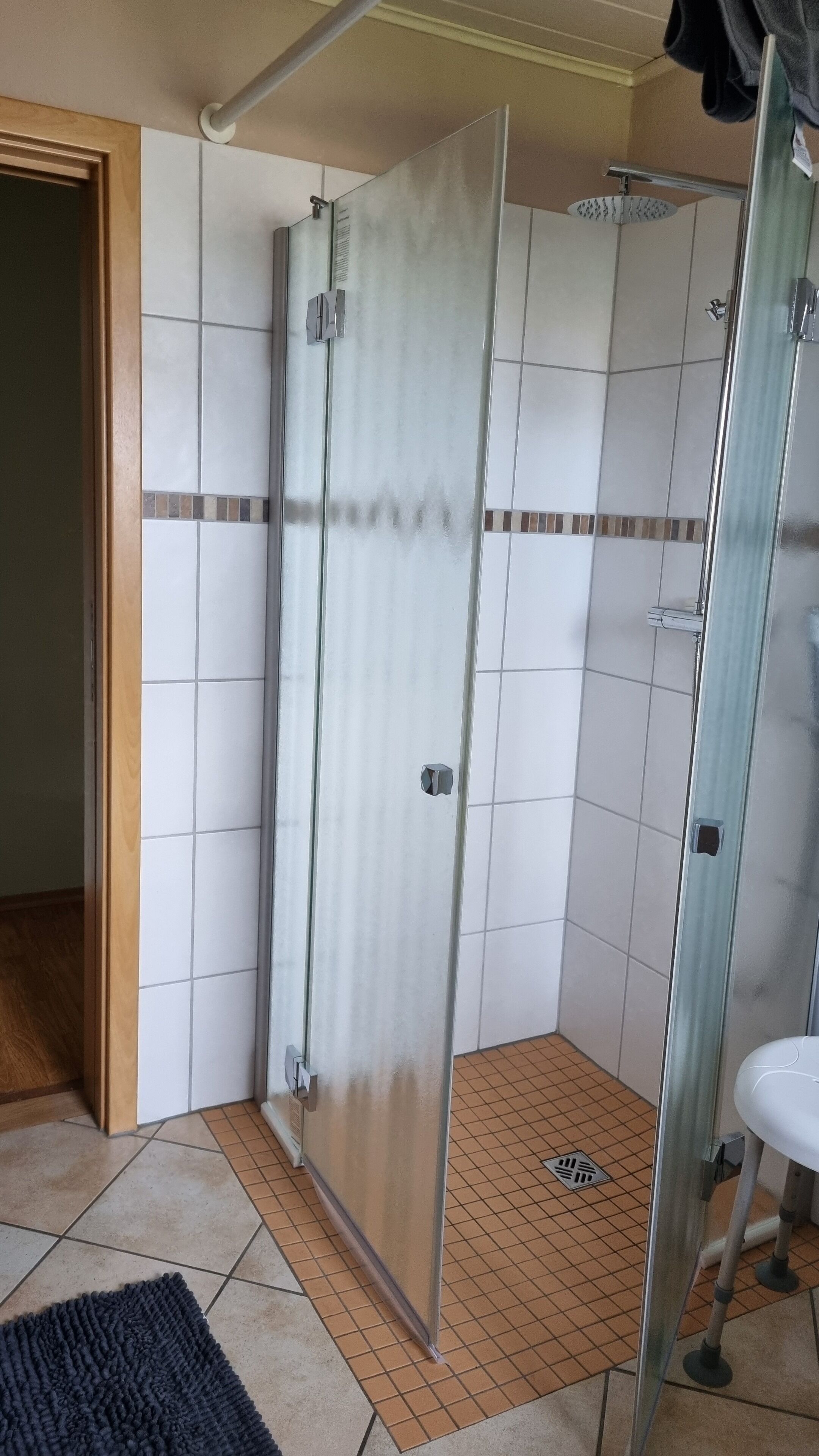 Une salle de bain avec une douche à parois de verre, des murs recouverts de carreaux blancs et un sol carrelé.