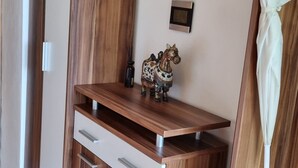 Una habitación con un armario de madera, un pequeño estante con adornos y un perchero.