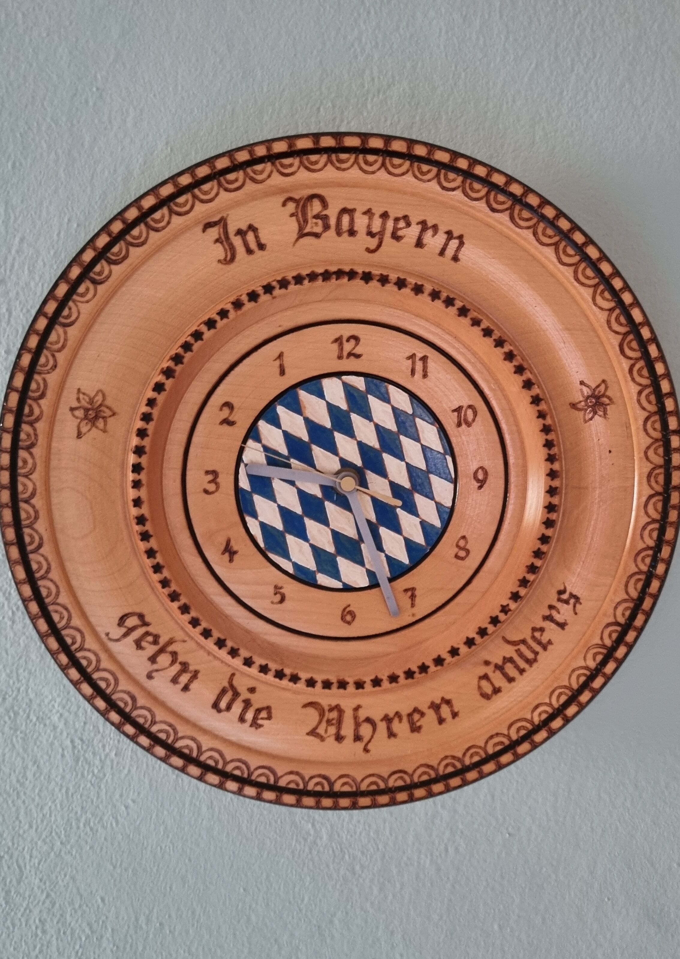 Un orologio in stile bavarese, caratterizzato da un motivo a scacchi e con la scritta 'In Bayern' e 'Gebt die Uhr an'.