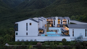 Un hotel moderno con diversi edifici, una piscina e uno sfondo montuoso.