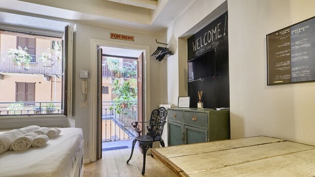 A room with a bed, a table, a chair, a balcony, and a welcome sign. - Urban Design Studio | Buenos Aires District (Milano)