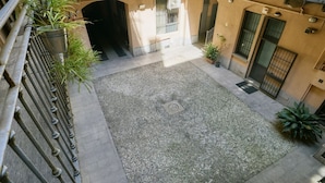 A courtyard with a gravel floor, potted plants, and a metal railing. - Urban Design Studio | Buenos Aires District (Milano)