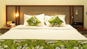 A hotel room with a neatly made bed, two pillows with floral designs, a nightstand with a phone and remote control, and a wall-mounted light. - Hotel RS Grand  (Agra)