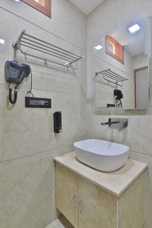 A bathroom with a white sink, a hairdryer, a towel rack, and a mirror. - Hotel RS Grand  (Agra)