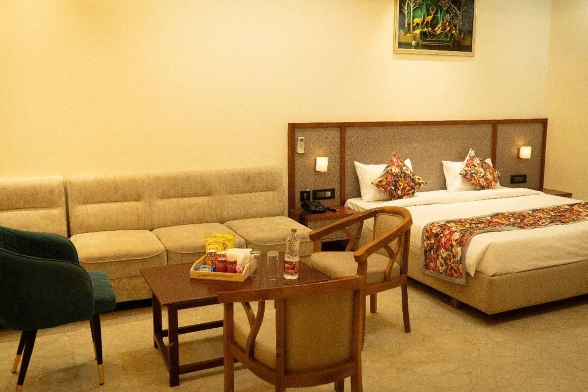 A hotel room with a bed, a sofa, a chair, a small table, and a painting on the wall.