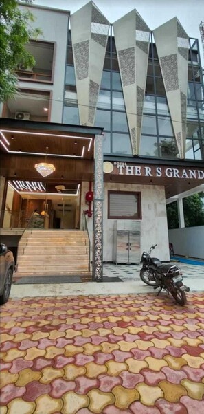 A hotel entrance with a modern design, featuring a staircase leading to the lobby, a motorcycle parked outside, and a patterned tile floor. - Hotel RS Grand  (Agra)