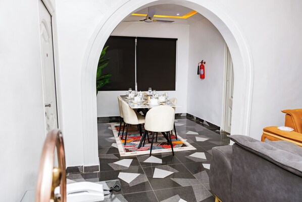 A dining area with a table set for four, a ceiling fan, and a fire extinguisher on the wall. - Bawuah Royal Apartments (Kumasi)
