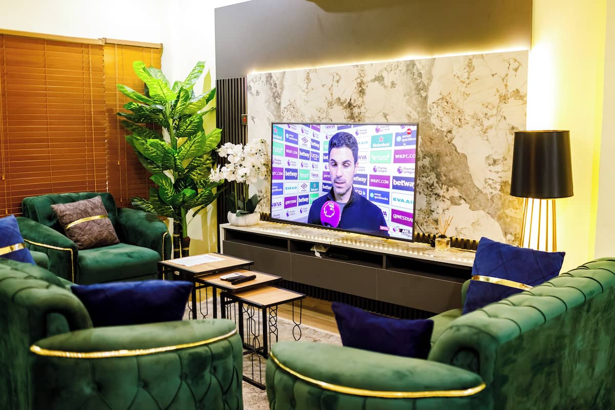 A modern living room with green upholstered sofas, a large flat-screen TV, and a decorative plant.