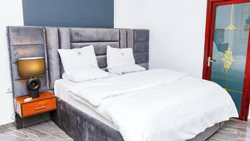 A modern bedroom with a large bed, a nightstand with a lamp, and a red-framed door.