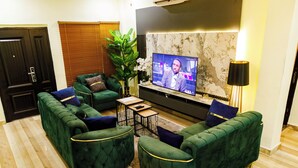 En moderne stue med grønne polstrede sofaer, et fladskærms-TV, et sofabord og en potteplante.
