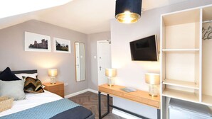 A hotel room with a bed, bedside tables with lamps, a desk with a chair, a TV mounted on the wall, and a wardrobe. - Ocho Homes By Eight Continents - R7 (Belfast)