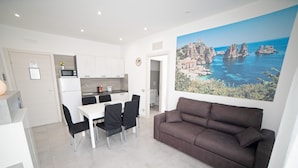 A modern living room with a brown sofa, a dining table with chairs, a kitchen area, and a large scenic painting on the wall. - City Life Palermo (Palermo)