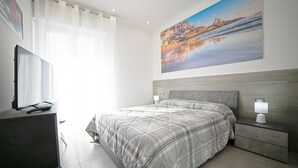 A bedroom with a large bed, a TV on a desk, and a painting of a coastal scene. - City Life Palermo (Palermo)