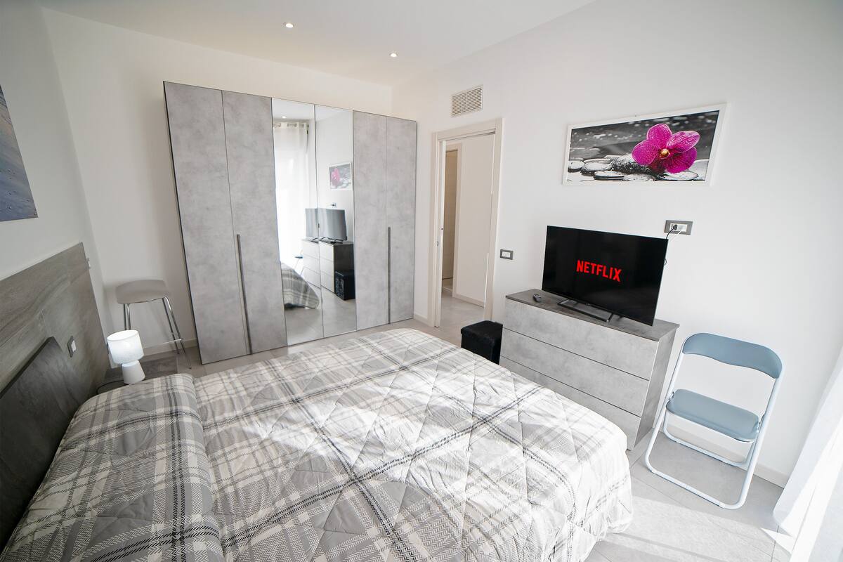 A modern bedroom with a large bed, wardrobe, and a TV displaying 'NETFLIX'.