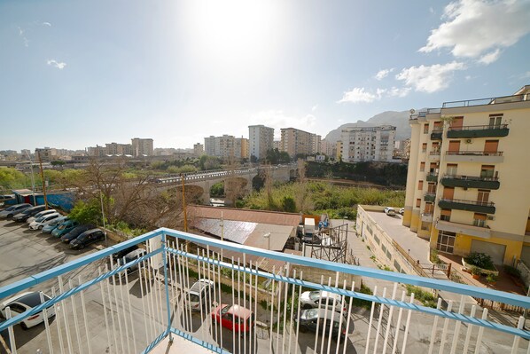 Blick vom Balkon auf einen Parkplatz mit mehreren Autos, eine Brücke und Wohnhäuser im Hintergrund.