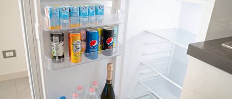 A refrigerator with multiple shelves stocked with beverages including juice boxes, soda cans, and bottled water.