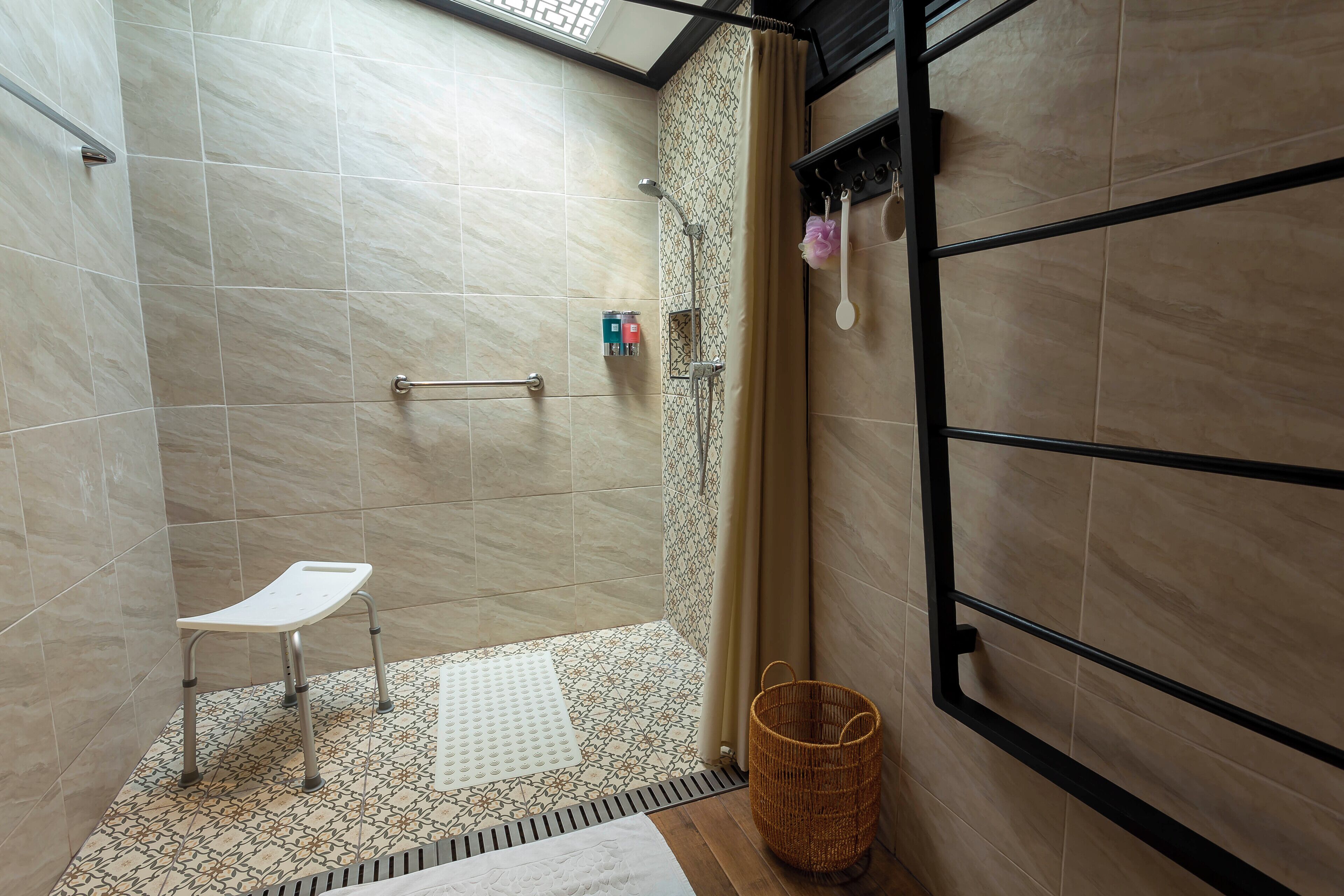 A shower area with a white chair, a patterned floor, and a basket.