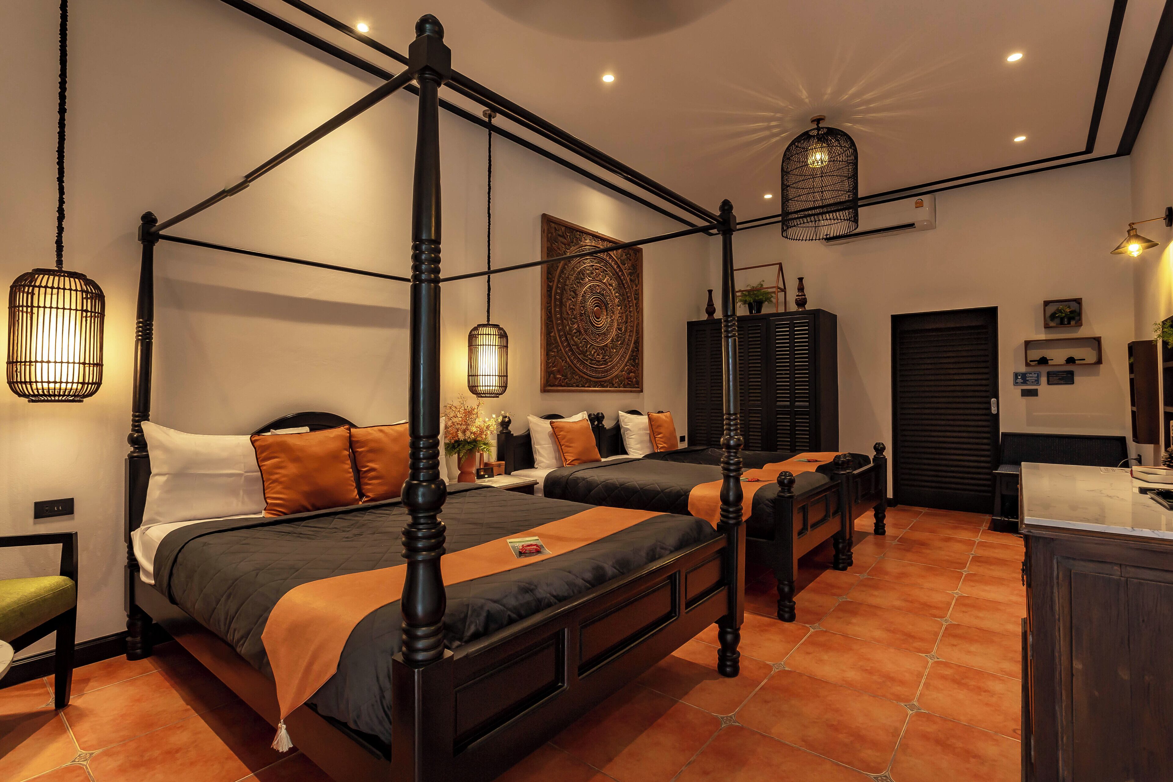 A four-poster bed with a dark finish, a green chair, and a small table with a vase of flowers.
