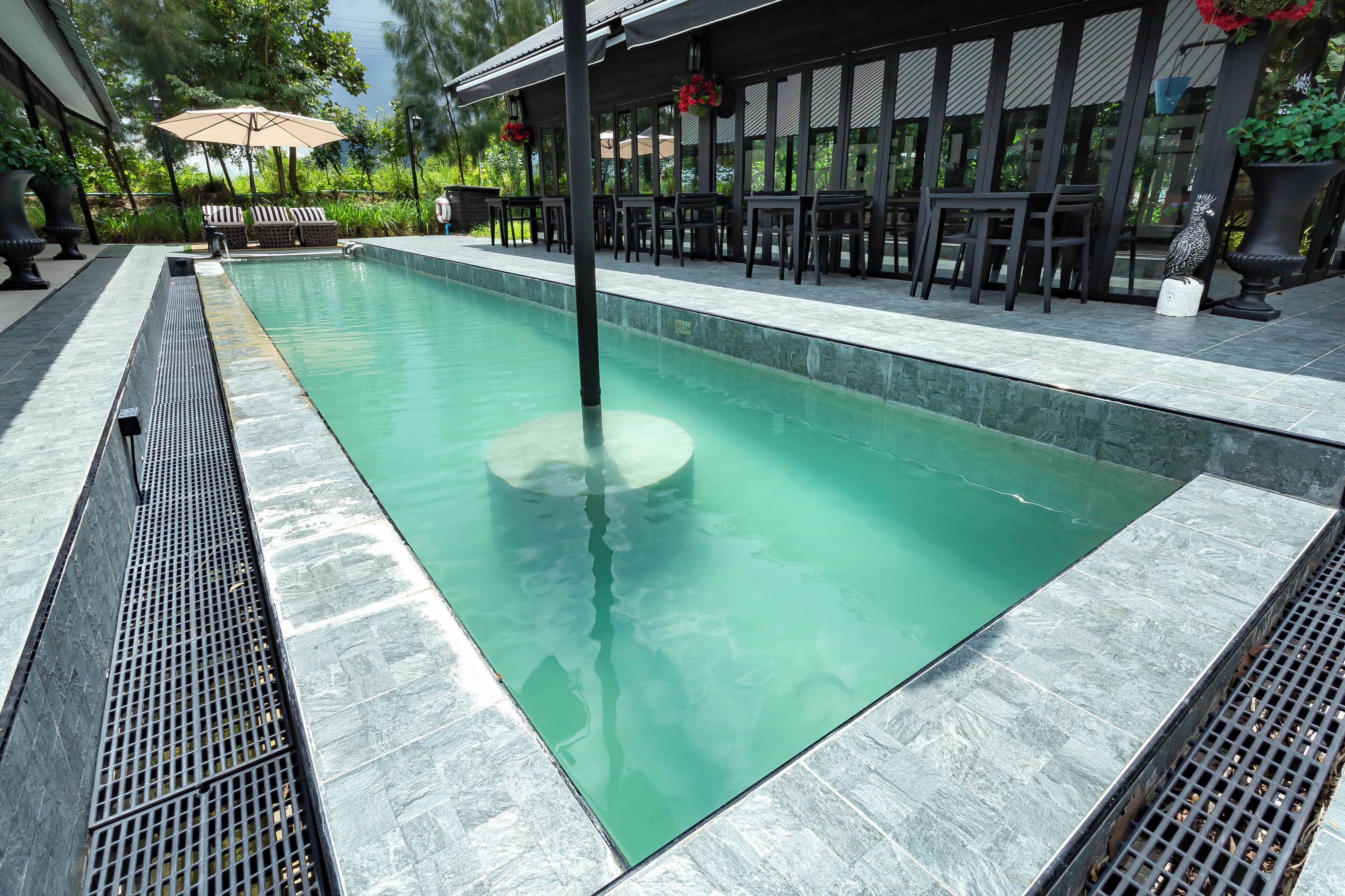 A swimming pool with a tiled deck, surrounded by outdoor seating and potted plants.