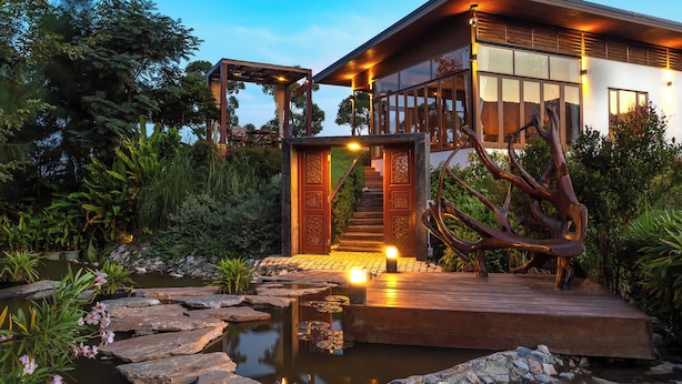 A modern house with a wooden deck, a small pond, and a staircase leading to the entrance.