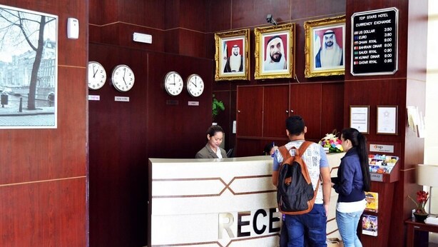 A hotel reception desk with clocks, framed portraits, and a currency exchange board. - Dancenter Top Star Heritage Village (Abu Dhabi)