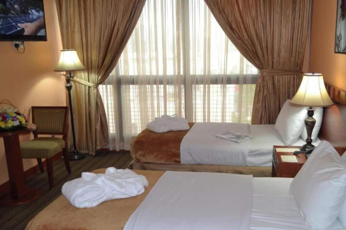 Una habitación de hotel con dos camas, una silla, una mesa con lámpara y una ventana con cortinas.