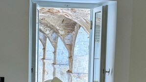 A room with two beds, each with a textured grey bedspread and rolled white towels. A door leads to an outdoor area with a stone structure.