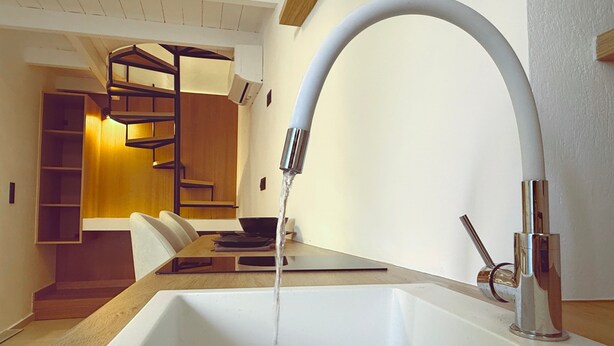 A modern kitchen with a large sink, a wooden dining table, and a built-in shelving unit.