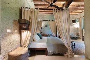 Un dormitorio rústico con cama, cortinas, una cesta tejida y un ventilador de techo.