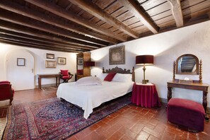 Une chambre à coucher avec un grand lit, un tapis rouge, un plafond en bois et une petite table avec une lampe.