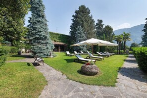 Un jardin avec un chemin en pierre, des fauteuils de jardin et un grand parasol.