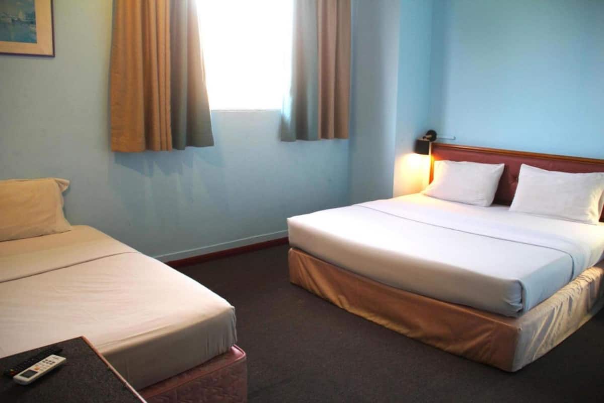 A hotel room with two beds, a small table with a remote control, and a window with curtains.