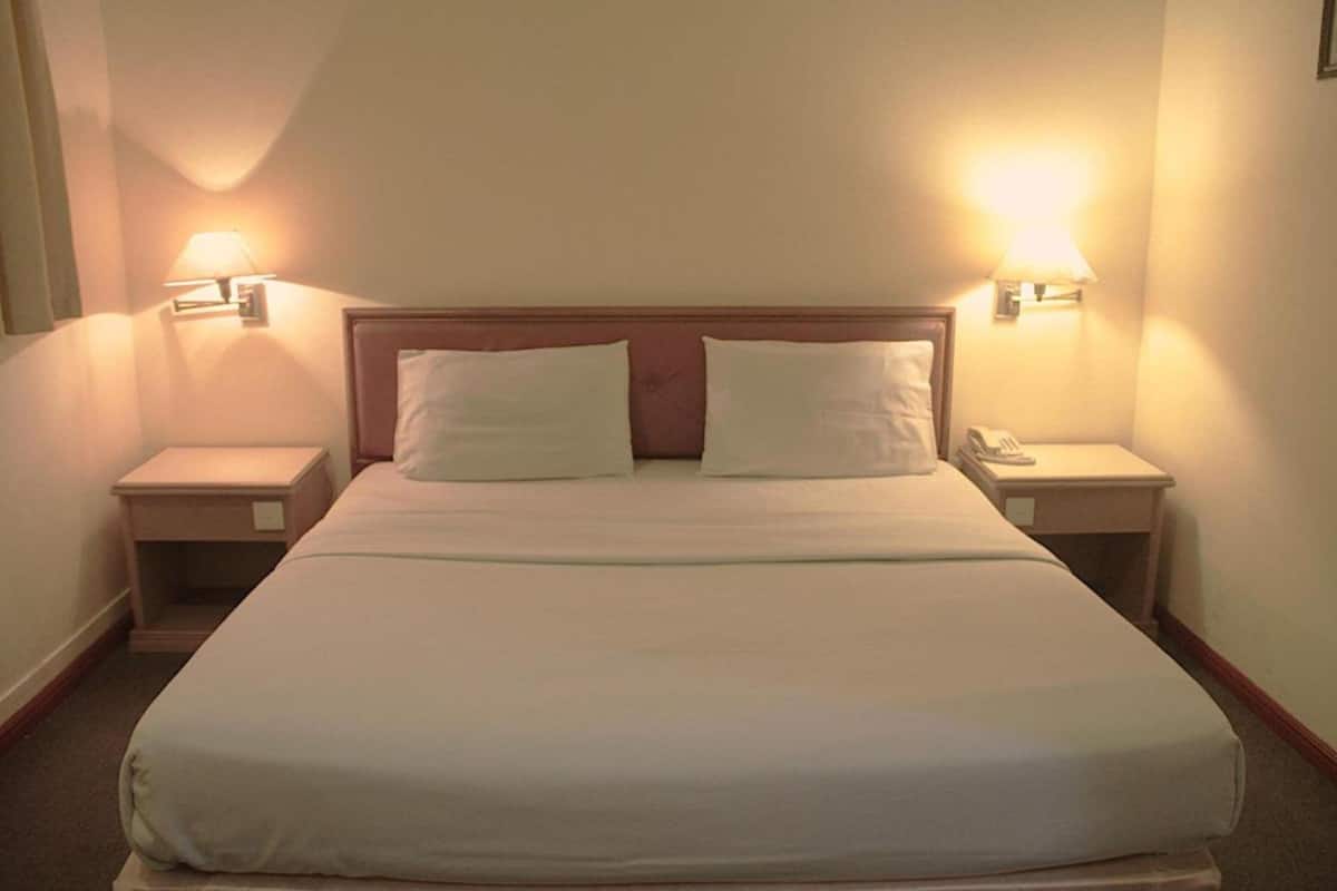 A hotel room with a large bed, two bedside tables, and two wall-mounted lamps.