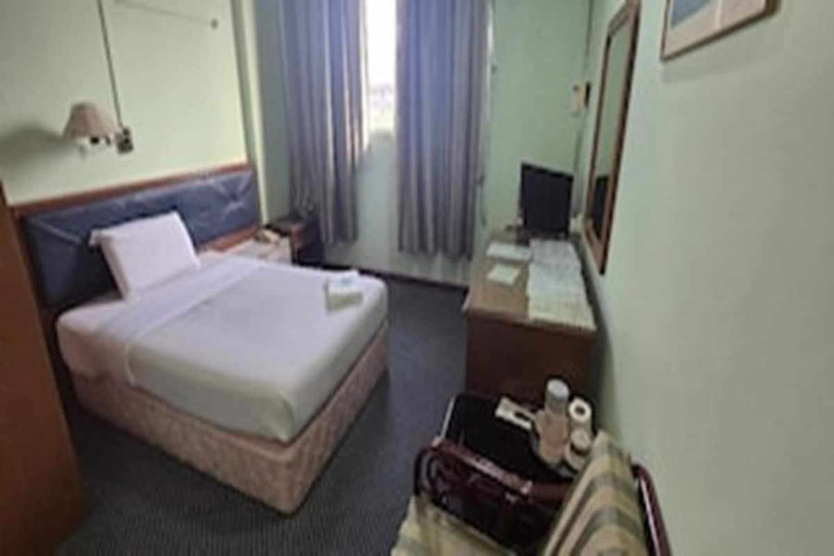 A hotel room with a bed, a desk with a computer, a chair, a lamp, and a window with curtains.