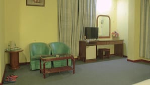 A room with a green sofa, a wooden desk with a television, a small table with a vase, and a mirror on the wall. - Hotel O Ramai (Sandakan)