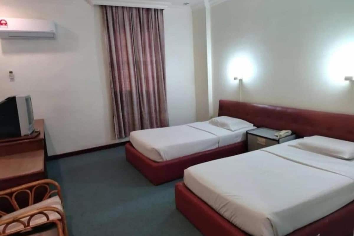 A hotel room with two beds, a desk, a chair, an air conditioning unit, a curtain, and two wall-mounted lights.