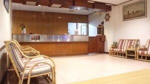 A reception area with a wooden reception desk, wicker chairs, and a large painting on the wall. - Hotel O Ramai (Sandakan)